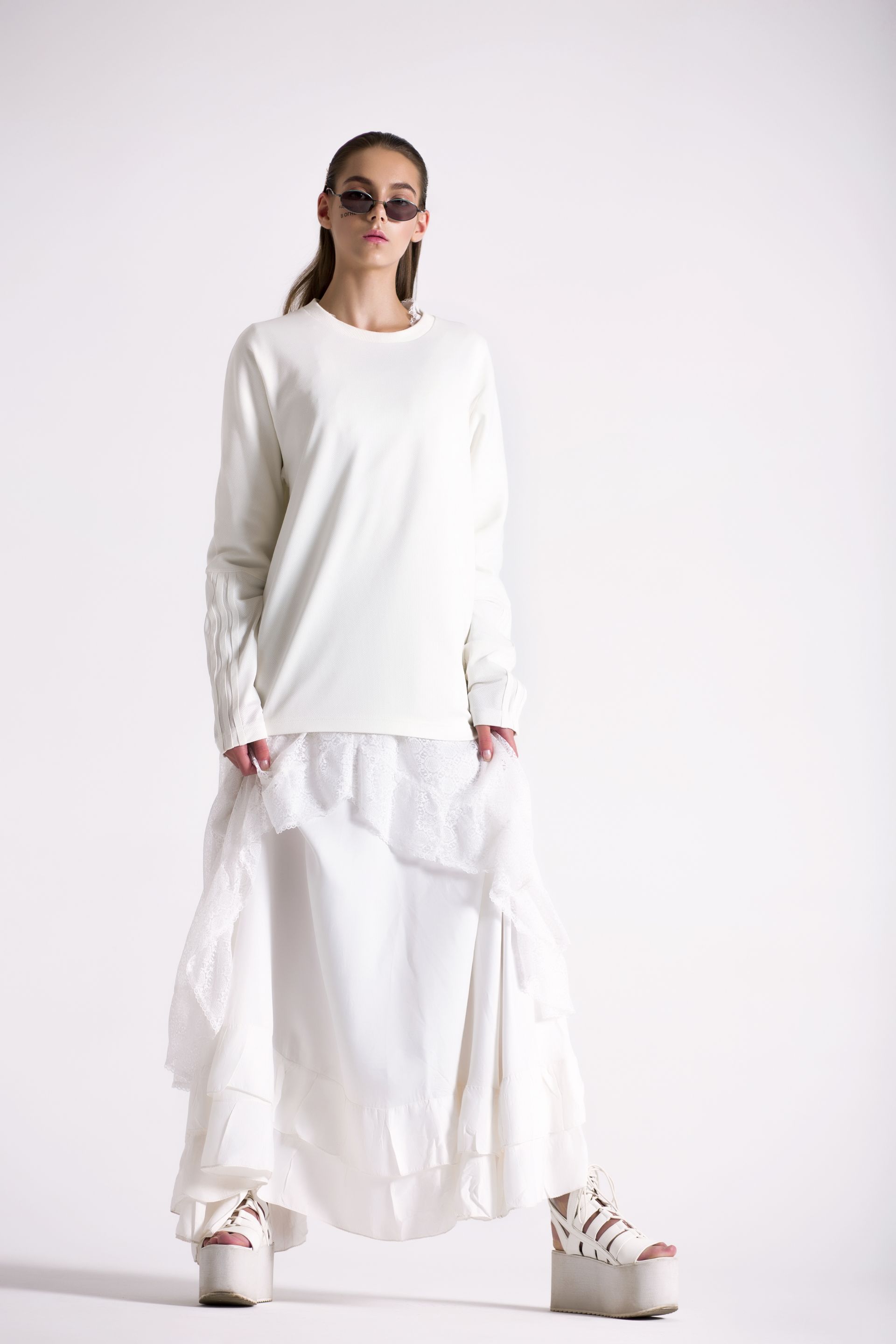 A woman wearing a white sweater and a white skirt is standing on a white background.