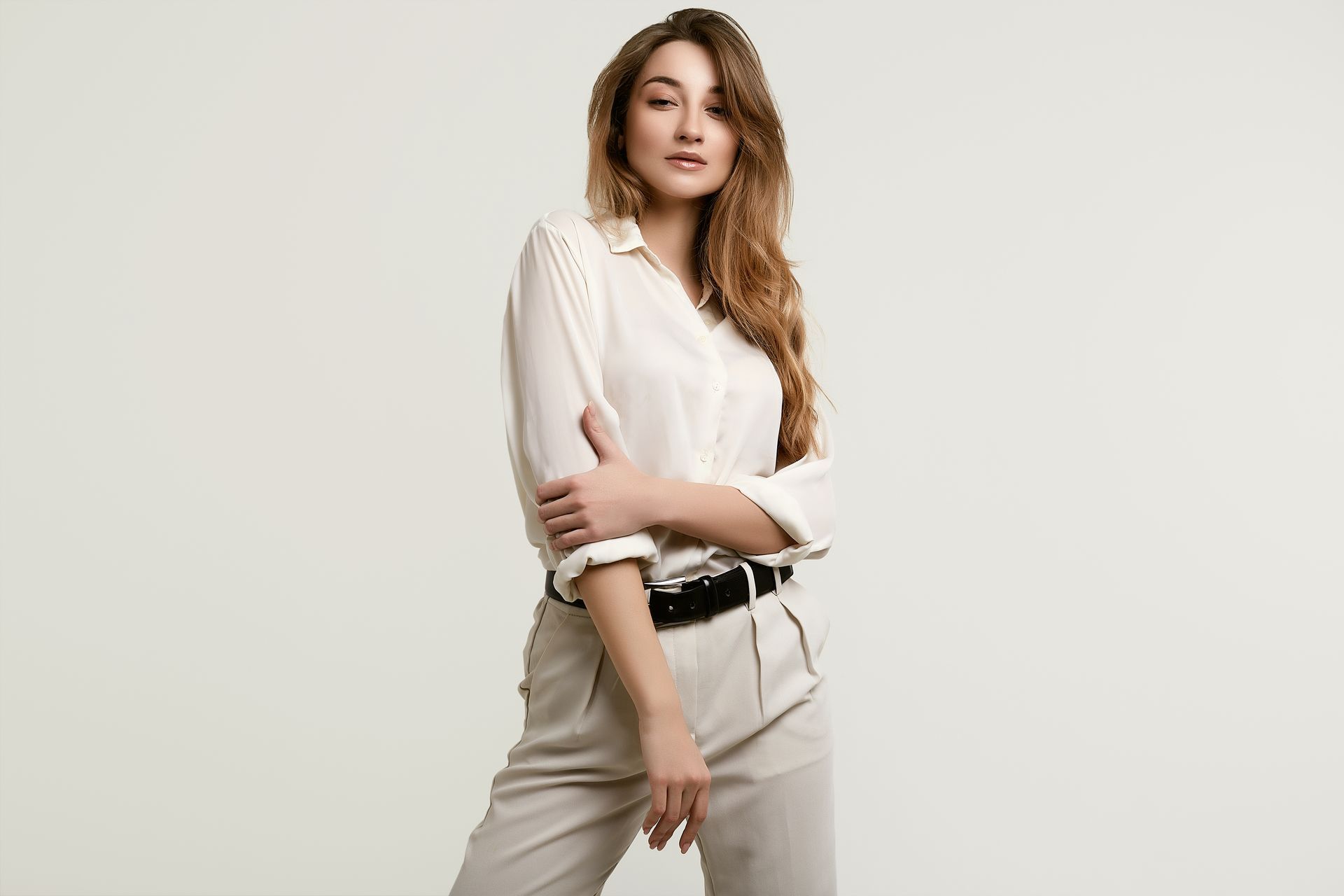 A woman in a white shirt and khaki pants is standing with her arms crossed.