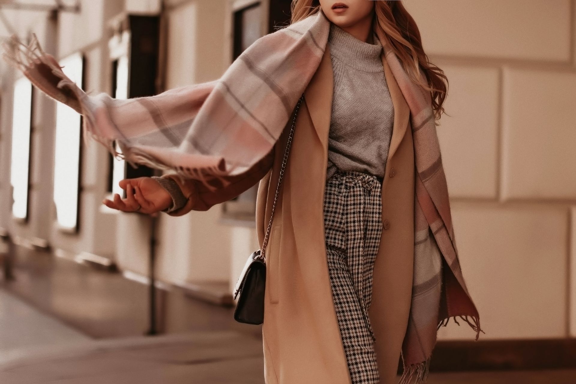 A woman wearing a plaid scarf and a coat is walking down the street.