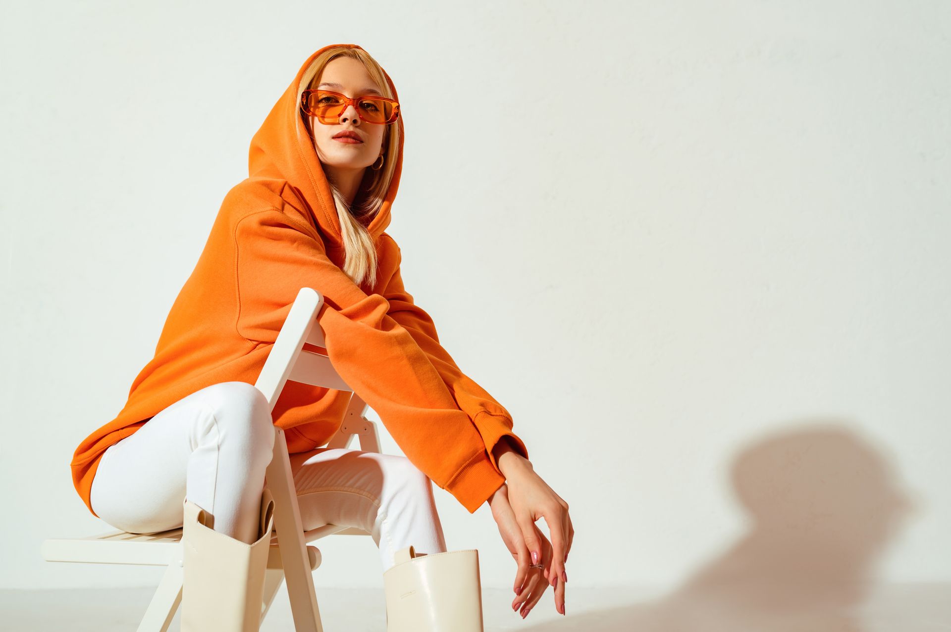 A woman in an orange hoodie and sunglasses is sitting on a chair.