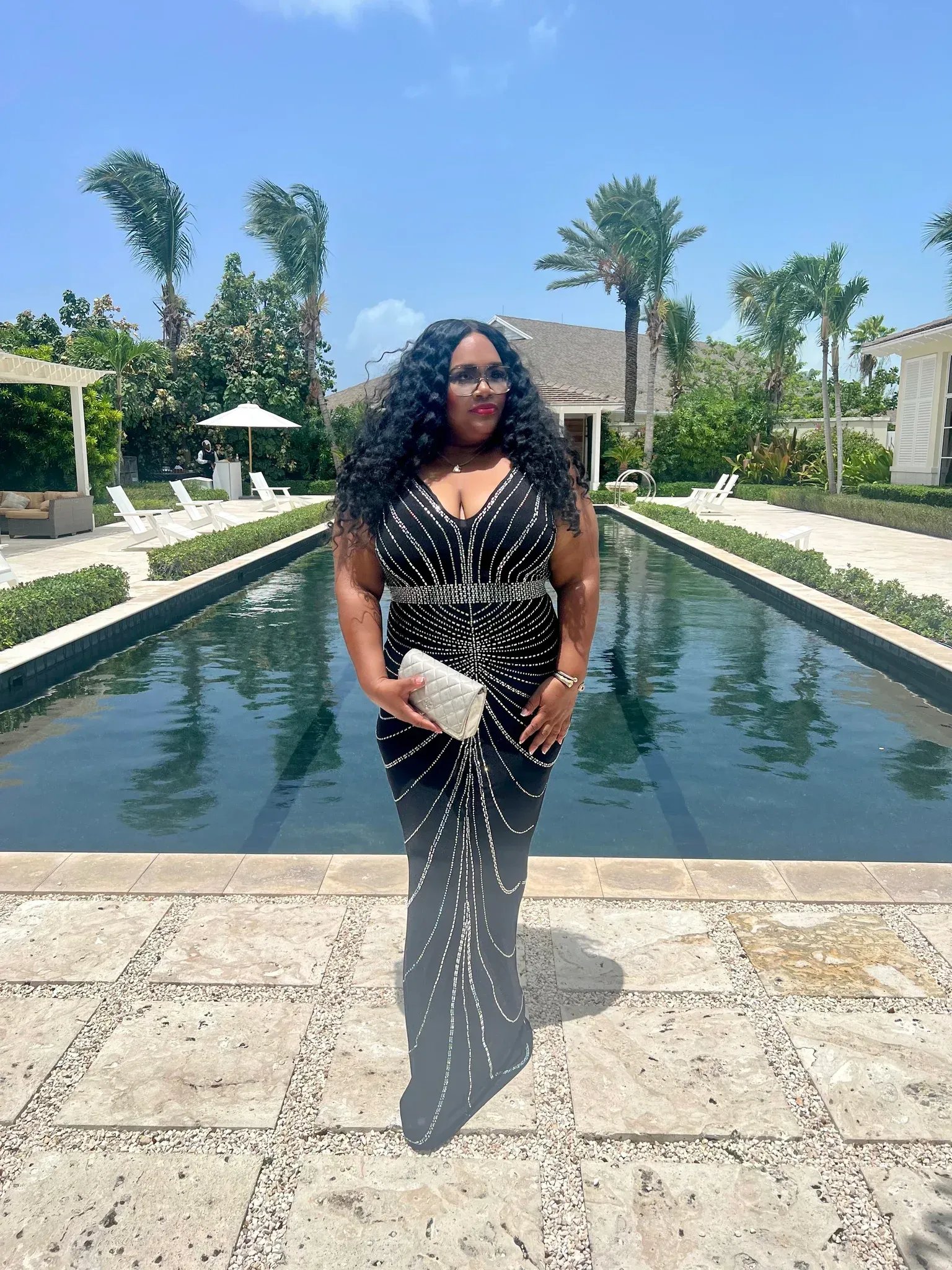 A woman in a black dress is standing in front of a pool.