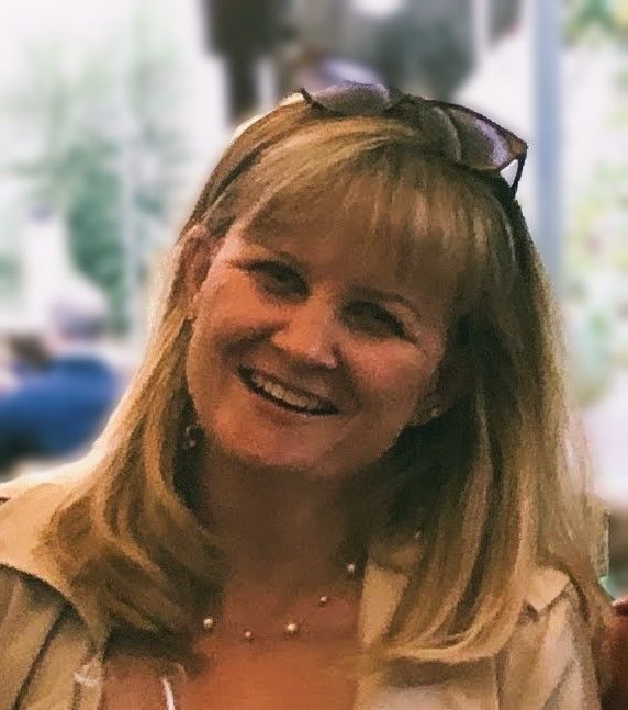 A woman wearing sunglasses and a pearl necklace smiles for the camera.