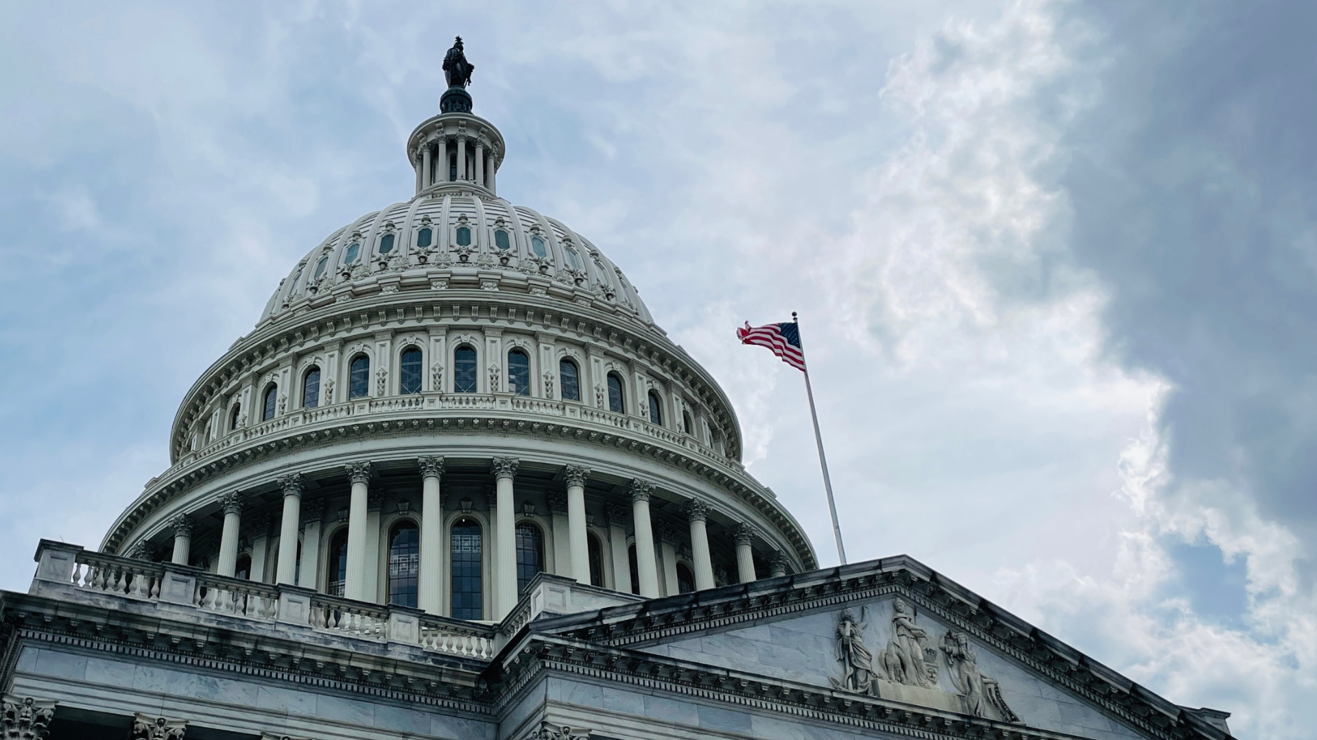 The dome of the capitol building with an american flag flying in front of it.