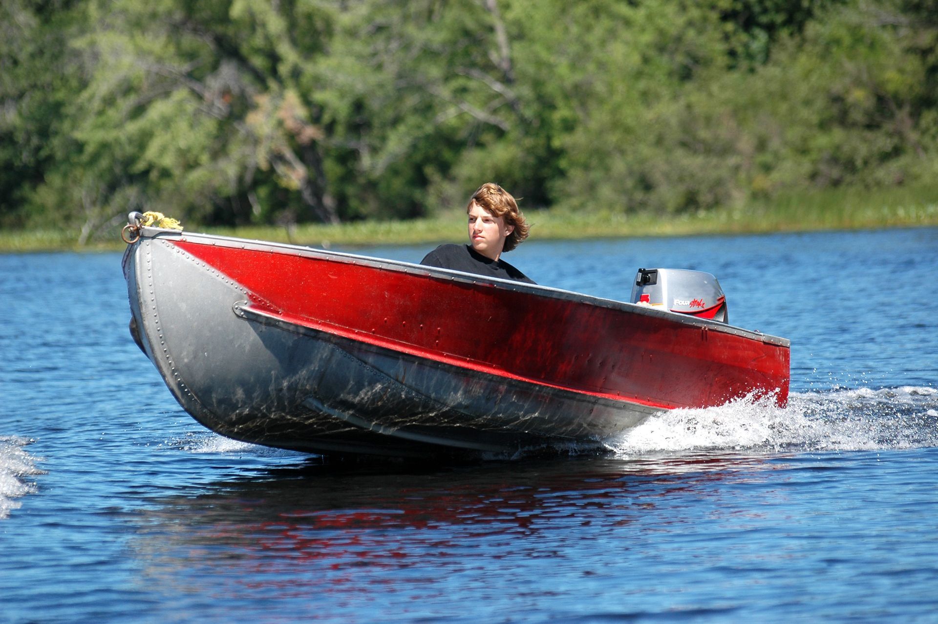 Image of red motorboat speeds across a lake, leaving a splash behind.