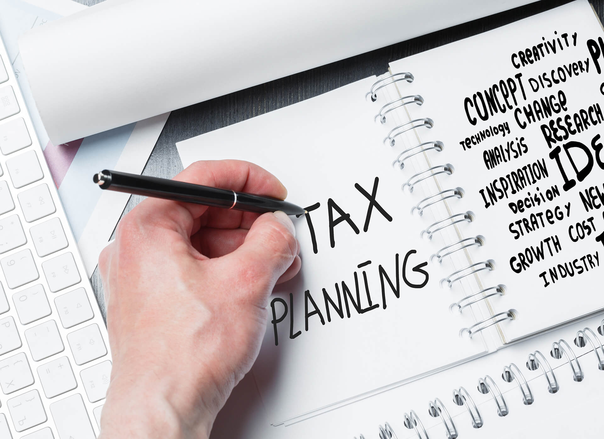 A person is writing tax planning in a notebook with a pen.