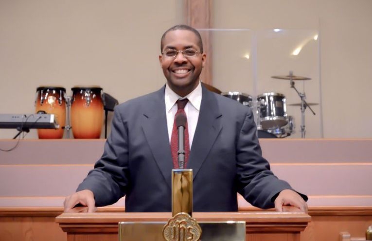 Man in suit smiles at lectern in church.