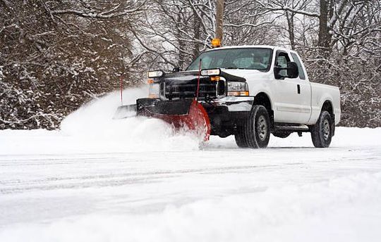 A white truck is plowing snow on a snowy road.