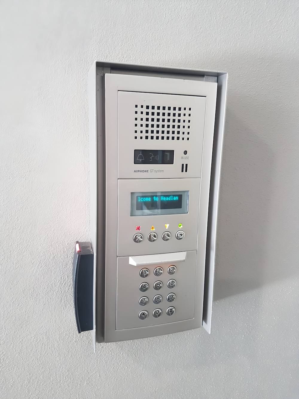 A Stainless-steel Door Phone With a Keypad is Hanging on a Wall — Adept Security In Corrimal, NSW