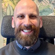 A bald man with a beard is smiling while sitting in a chair.