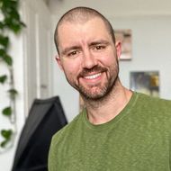 A man with a beard is wearing a green shirt and smiling for the camera.