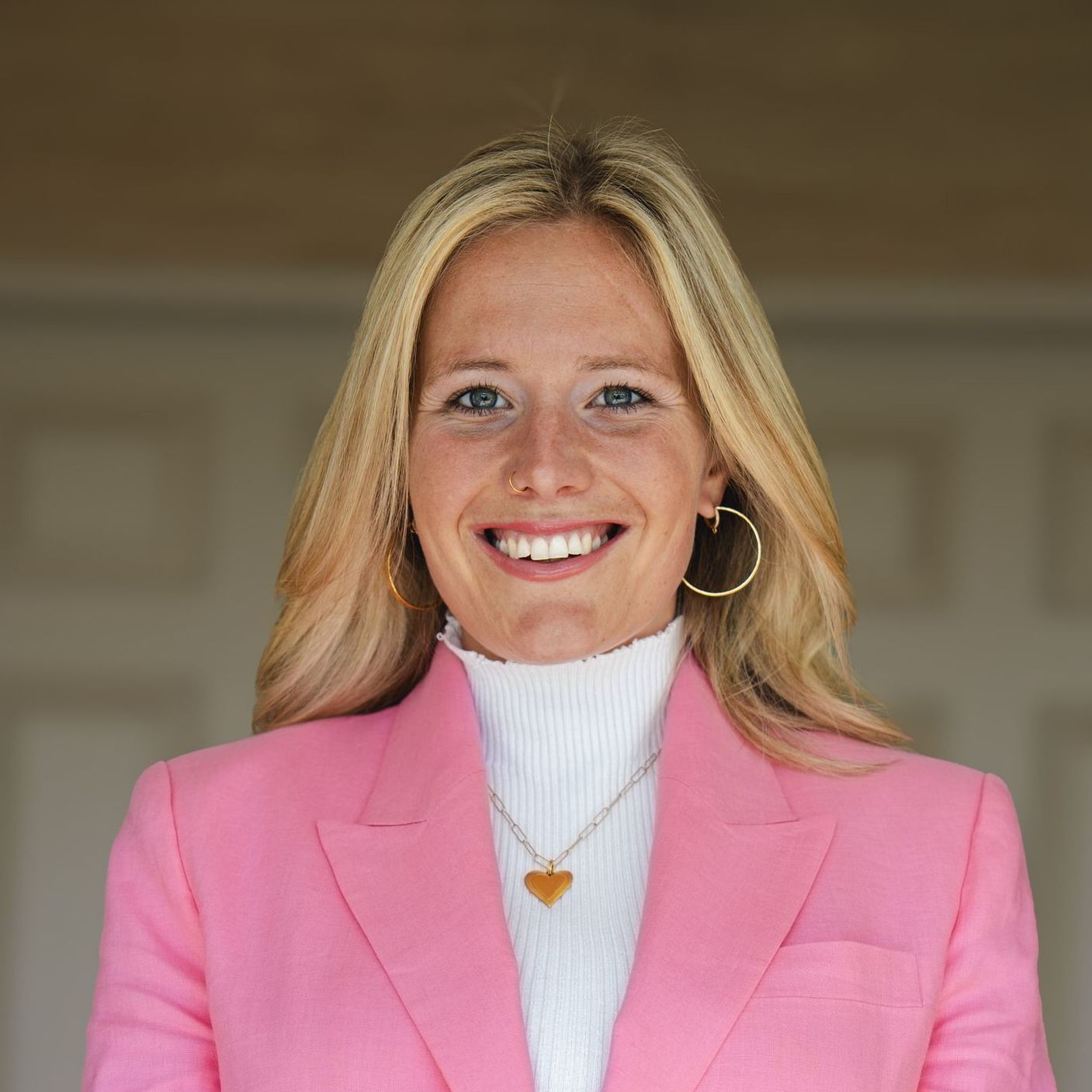 A woman in a pink jacket and white sweater is smiling for the camera.