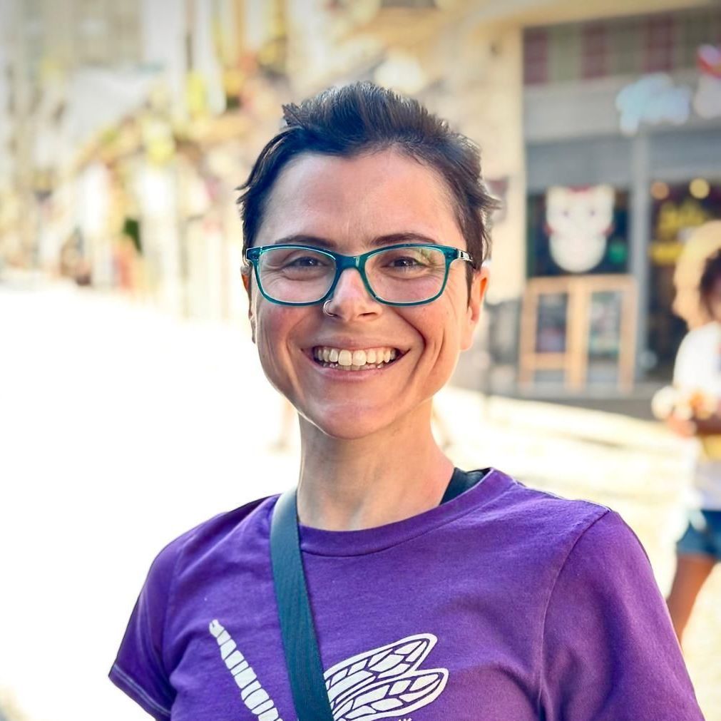 A woman wearing glasses and a purple shirt is smiling.