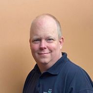 A bald man wearing a blue shirt is smiling for the camera.