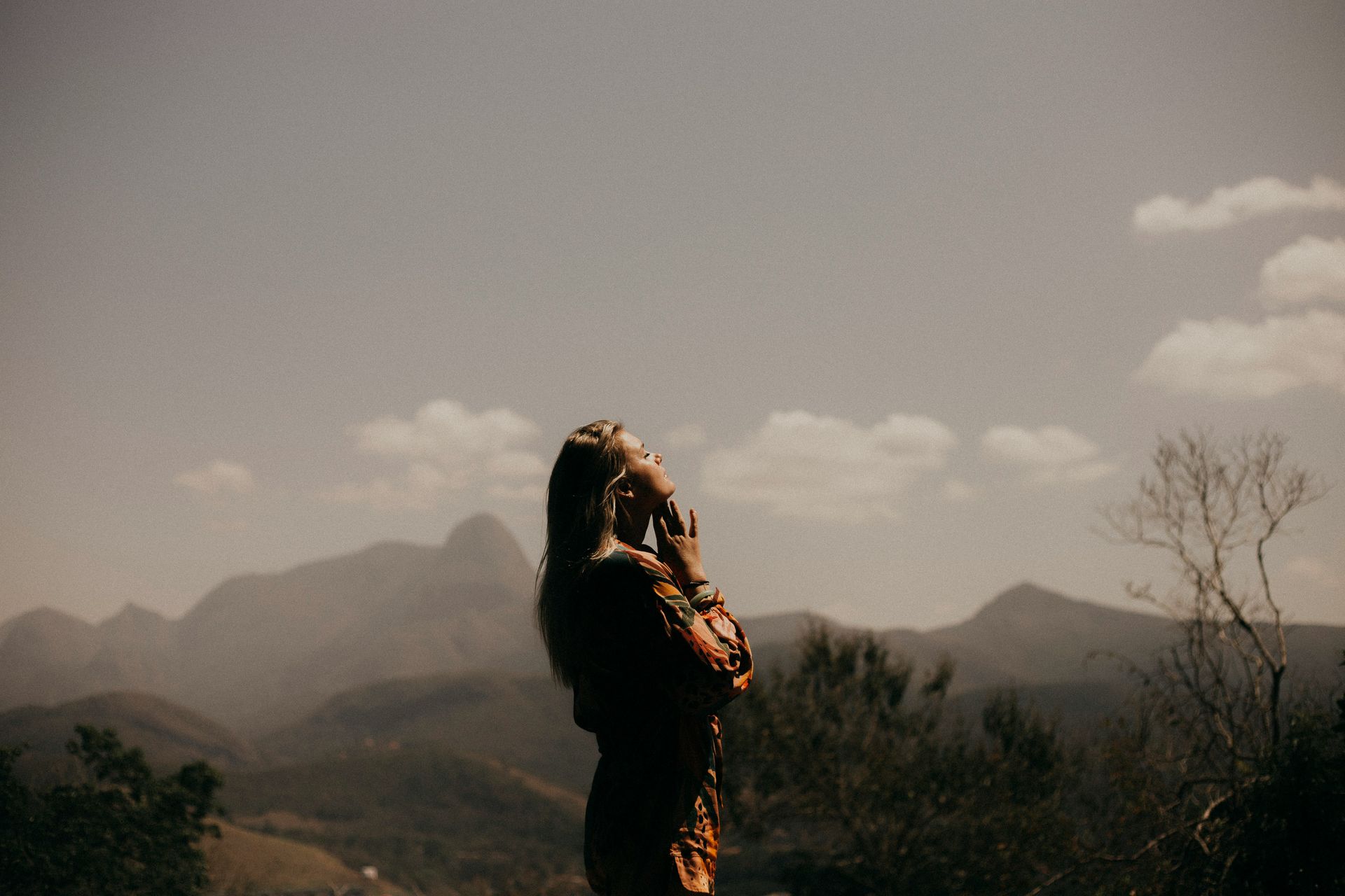 Woman stood with a mountain behind her with her hands under her chin 