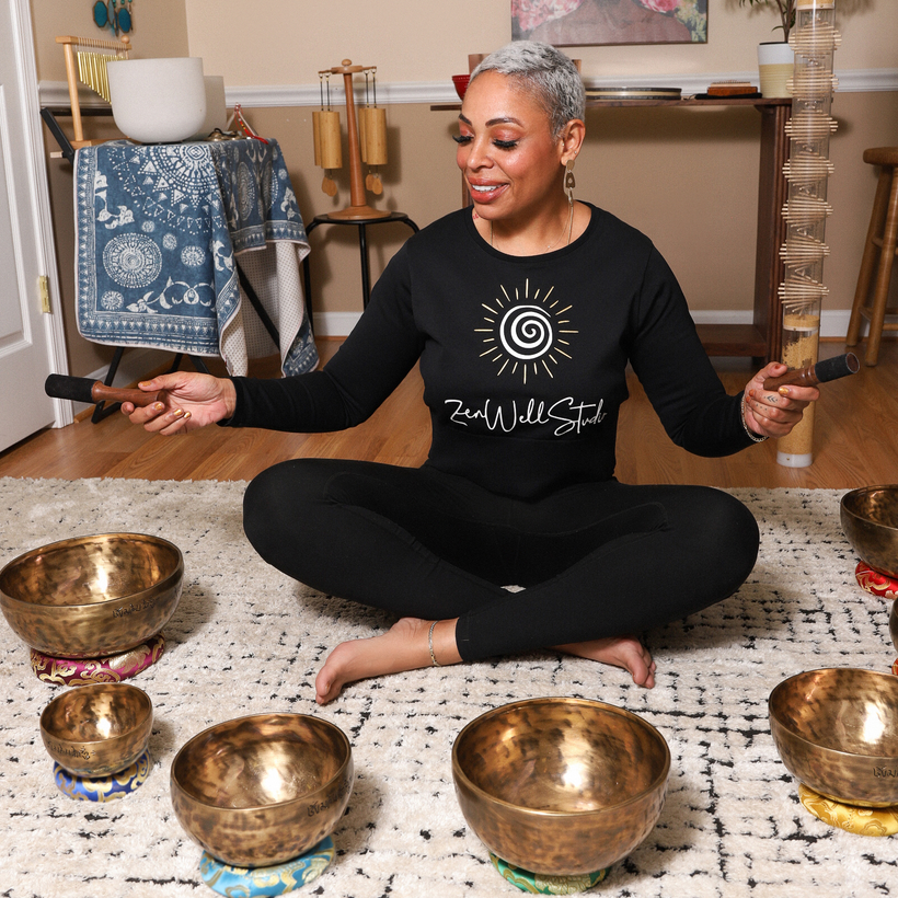 A woman in a black shirt is sitting on the floor playing singing bowls