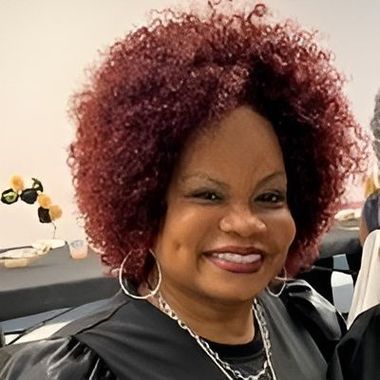 A woman with red curly hair and earrings is smiling for the camera.