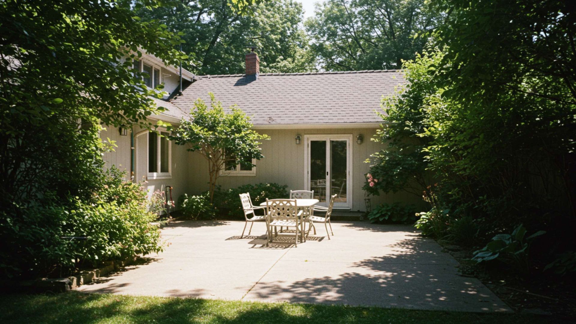 Patio with outdoor furniture in front of a house, surrounded by trees.