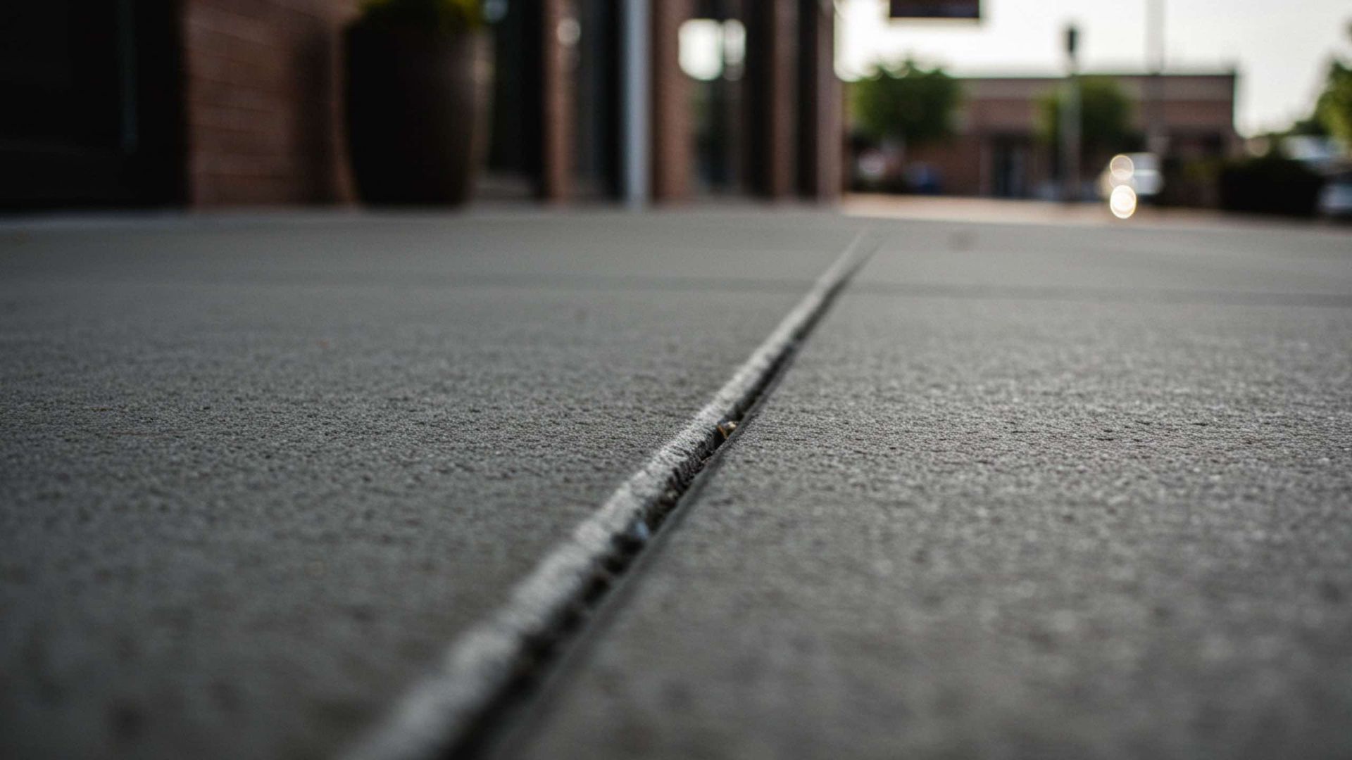 Close-up of a concrete sidewalk with a long crack running down the center, in front of a building.