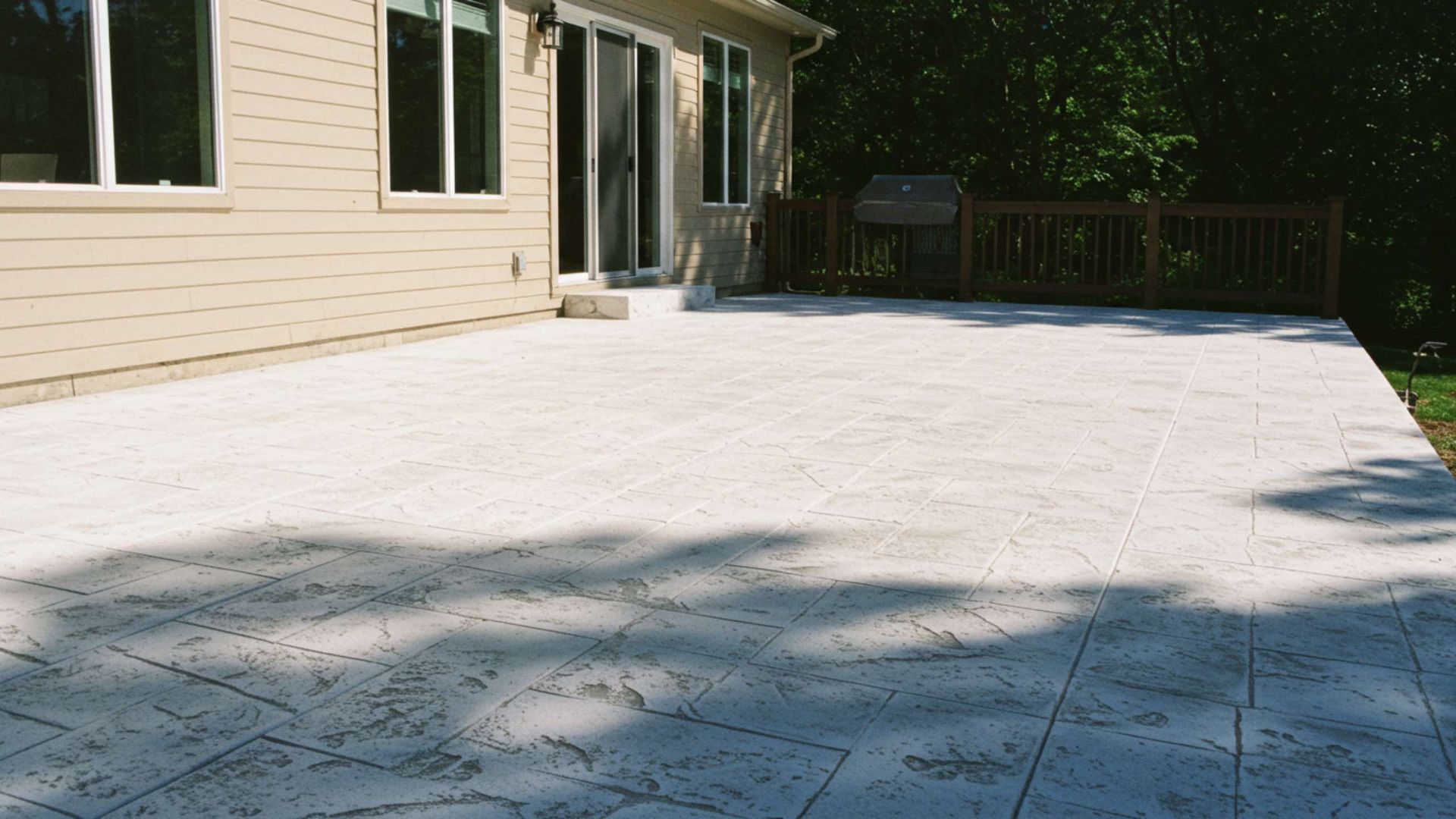 Beige composite deck attached to a house with sliding glass door. A grill is in the background.