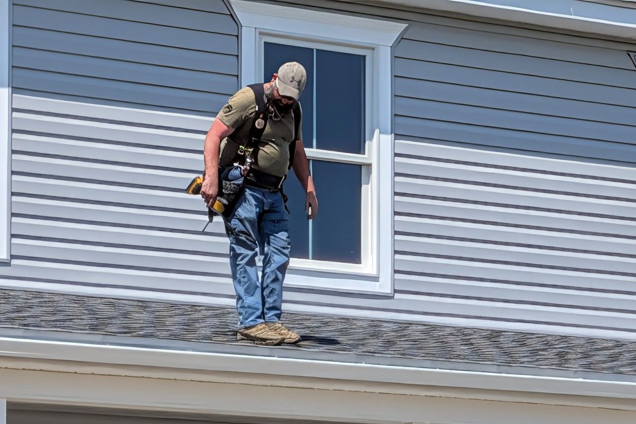 Worker inspecting a white downspout under a house eave, viewed from below.