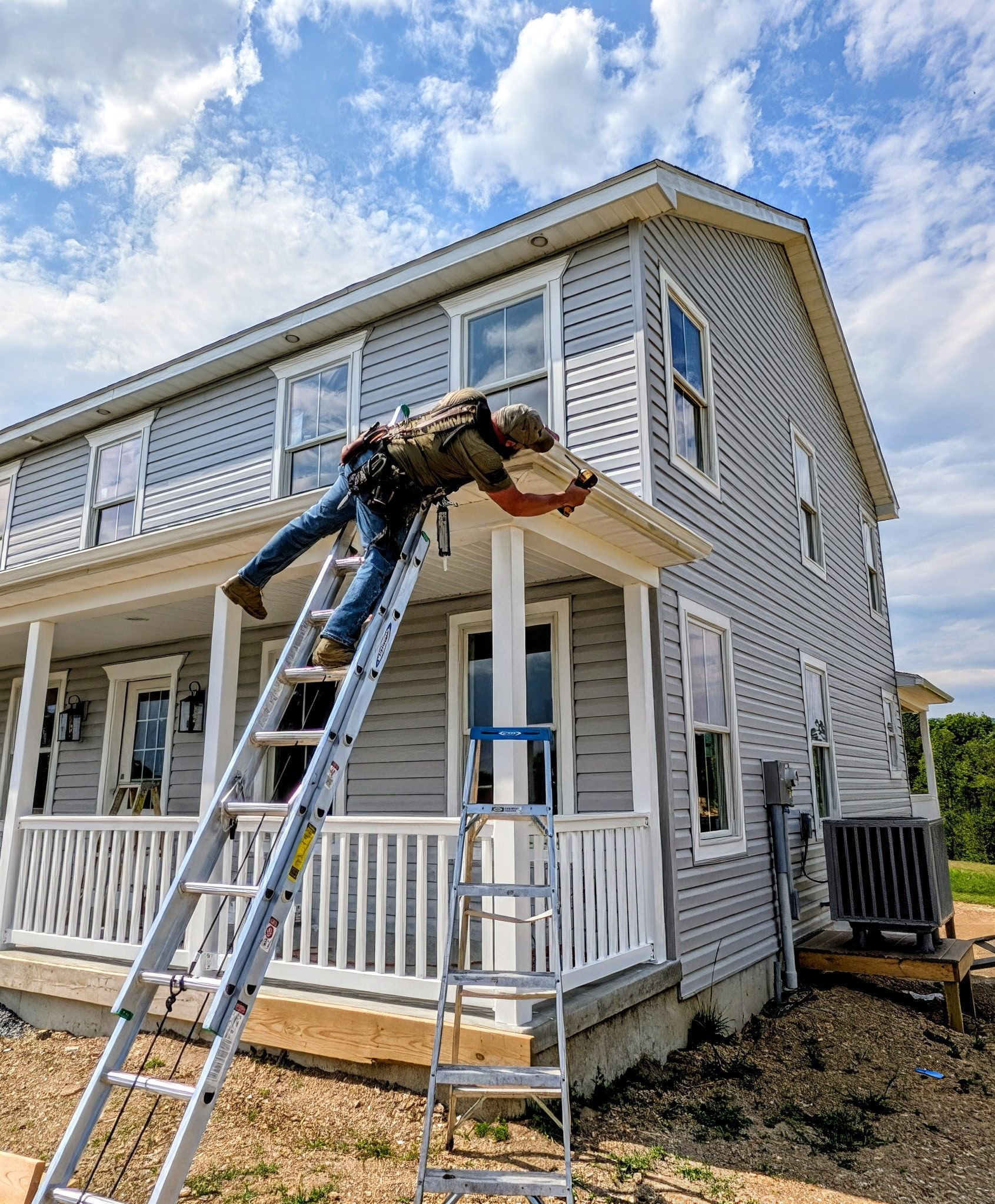 Exterior of a house with white walls, brown roof, windows, and gutters against a blue sky.