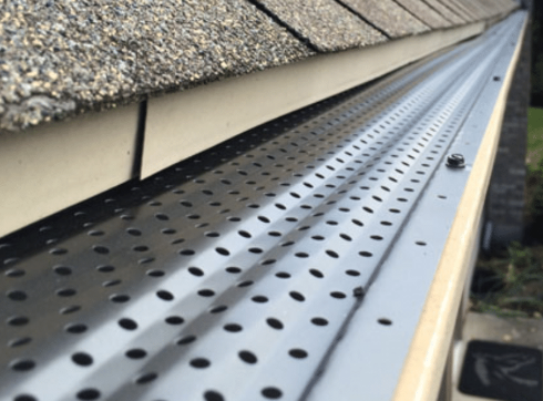 Gloved hand installing a white perforated drip-edge flashing under brown roof shingles.