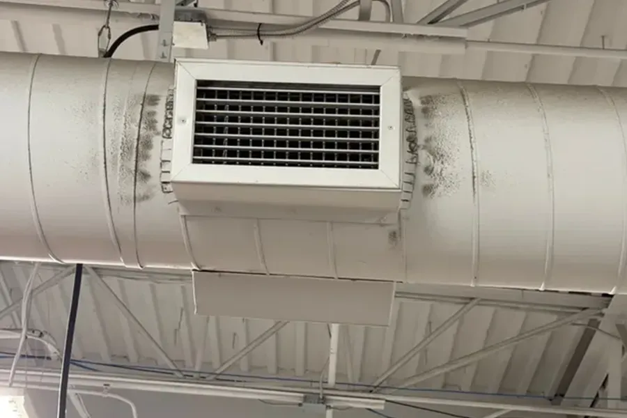 Ceiling air vent mounted on large white ductwork in an industrial interior