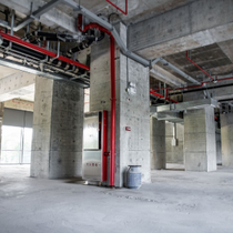 Empty concrete construction interior with exposed pipes, pillars, and unfinished ceilings