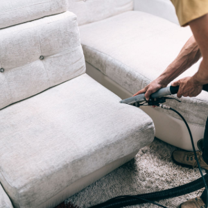 Person vacuuming a light gray sofa in a living room