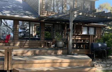 A large house with a wooden deck and a grill in front of it.