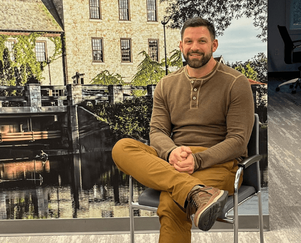 A man is sitting in a chair with his legs crossed in front of a wall mural.