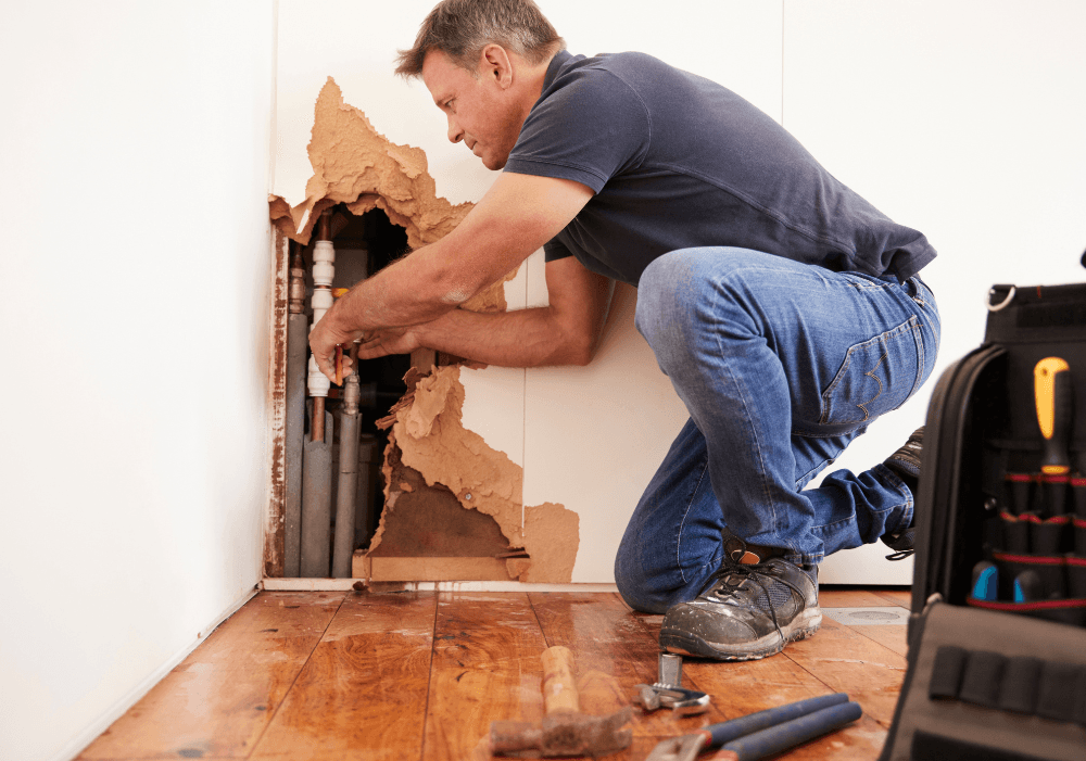 A man is kneeling on the floor fixing a hole in the wall.