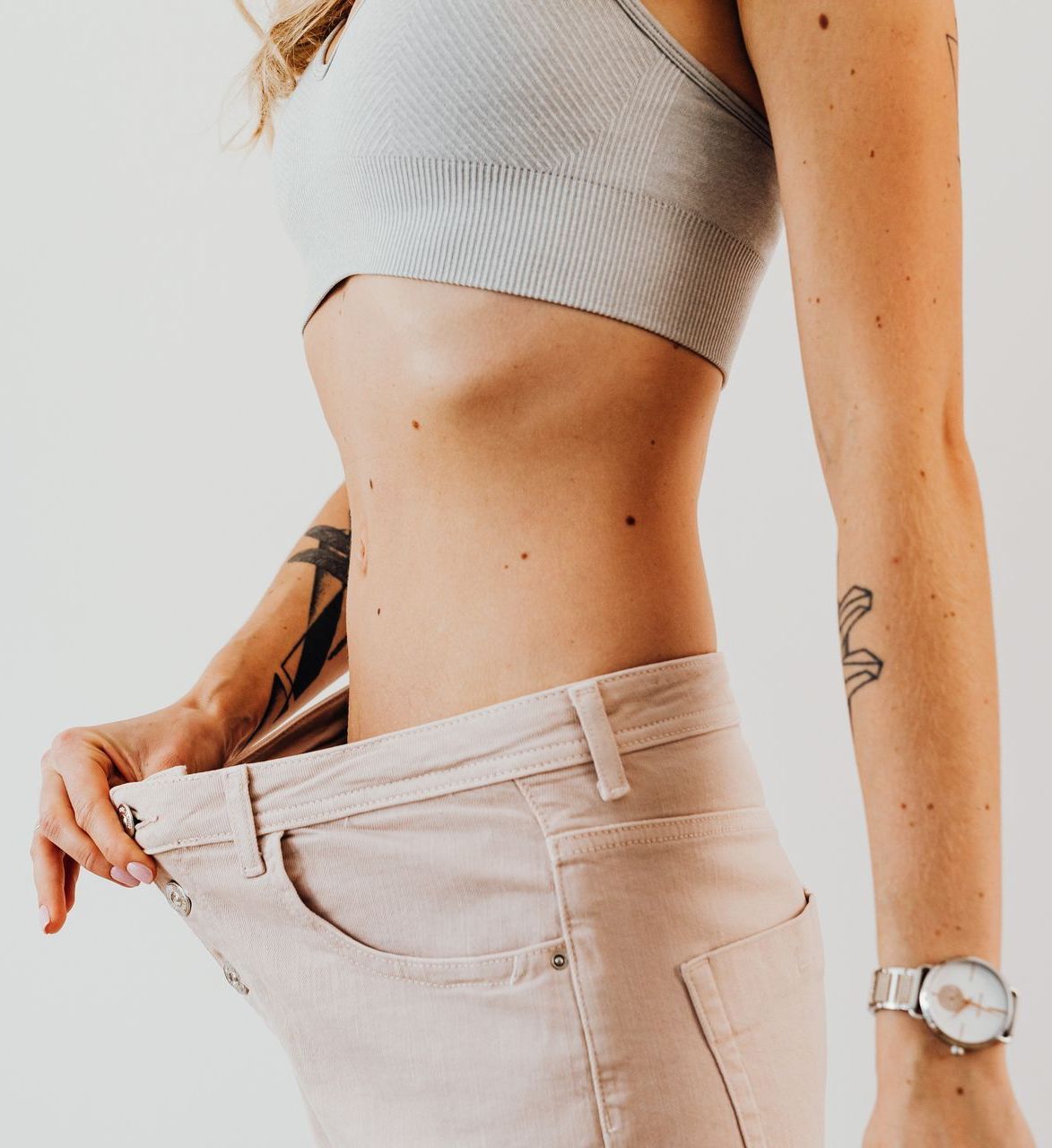 A slim woman with a tattoo on her arm is wearing a watch and a crop top and large pants.