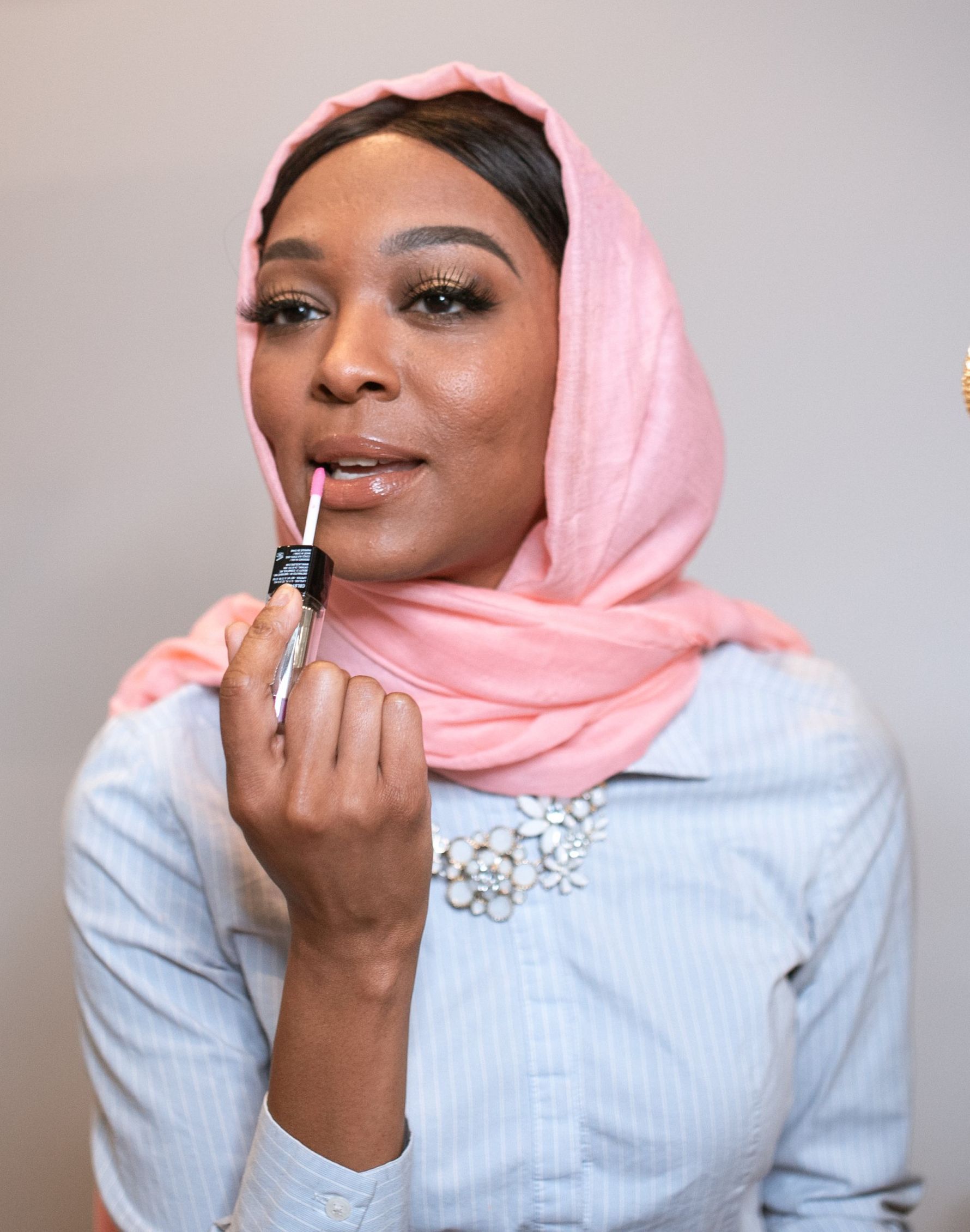 A woman wearing a pink scarf is applying lipstick to her lips