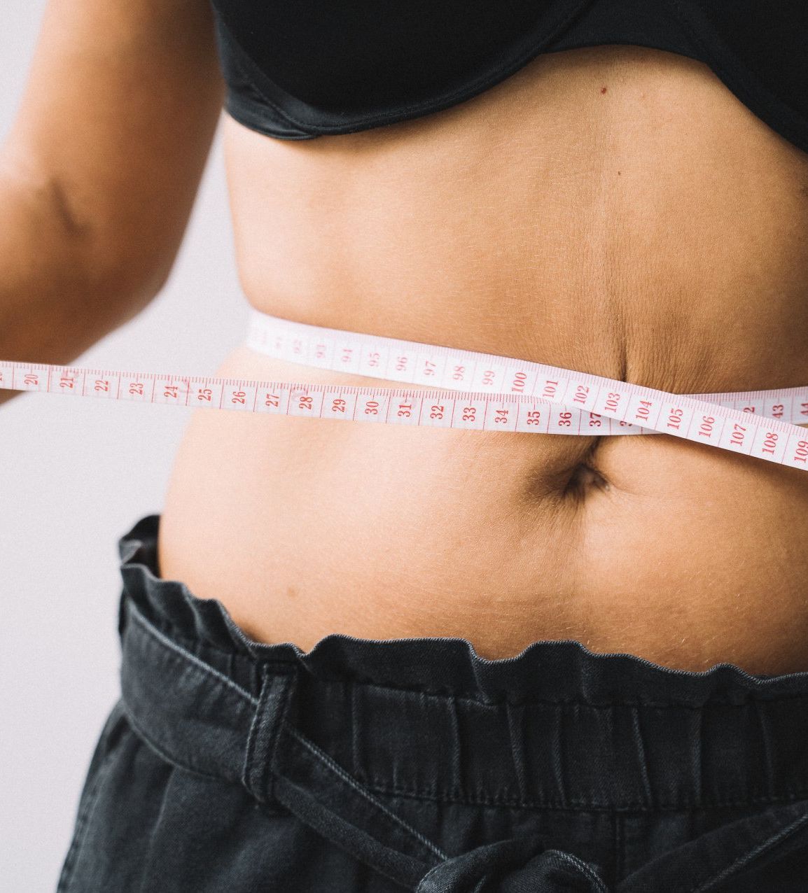 A woman is measuring her waist with a tape measure.