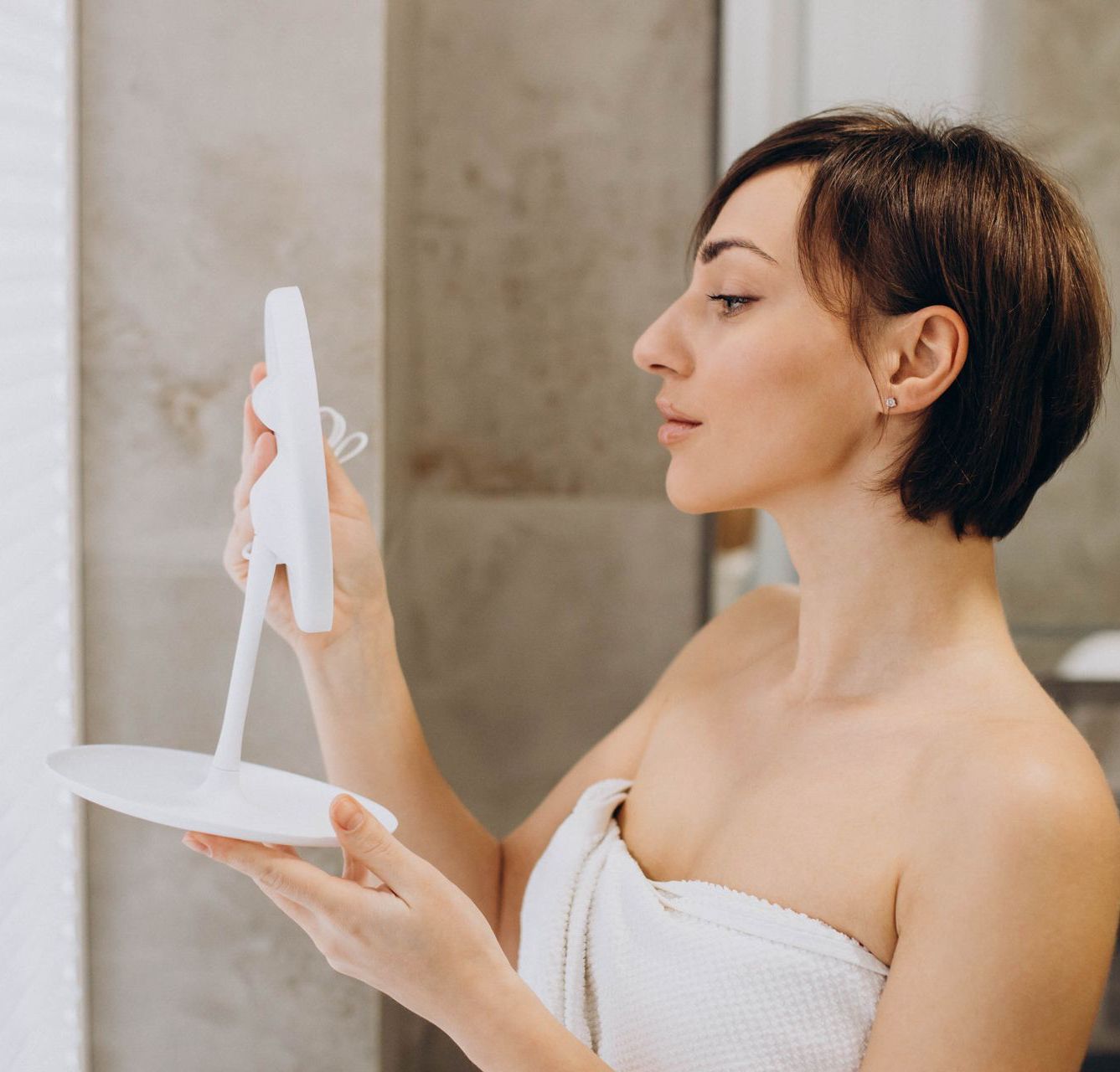 A woman wrapped in a towel is looking at her face in a mirror.