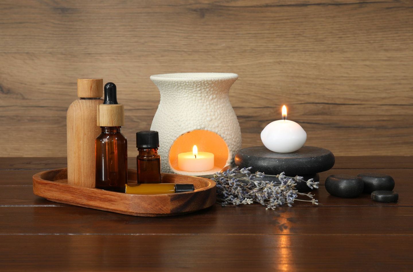 a wooden table topped with bottles of essential oils, a candle, and rocks