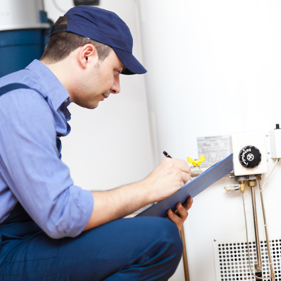 A man is writing on a clipboard in front of a water heater