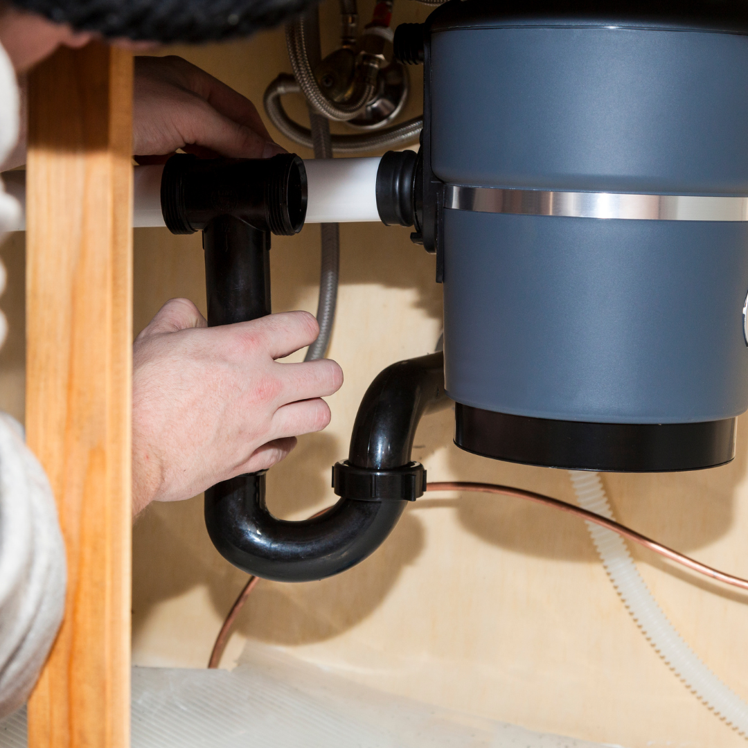 A man is fixing a garbage disposal under a sink