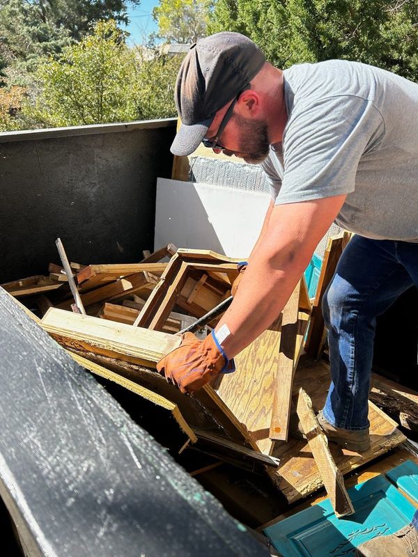 A man is working on a pile of wood in a dumpster.