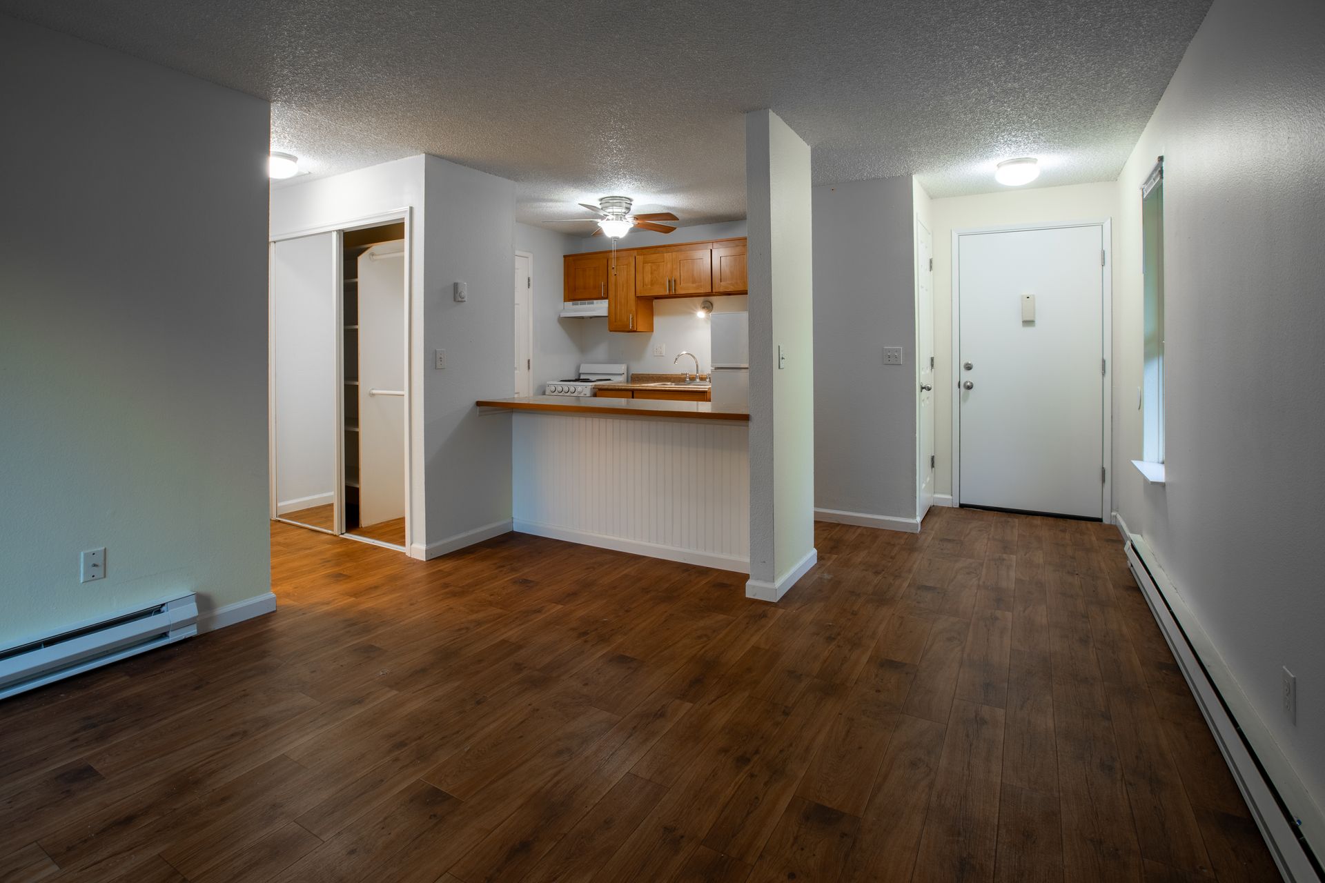 Empty apartment interior with kitchen, entryway, and hardwood floors.