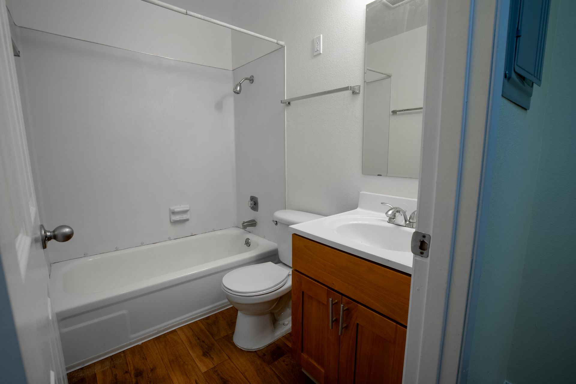 Bathroom with white tub, toilet, and vanity; wooden floor and blue wall.