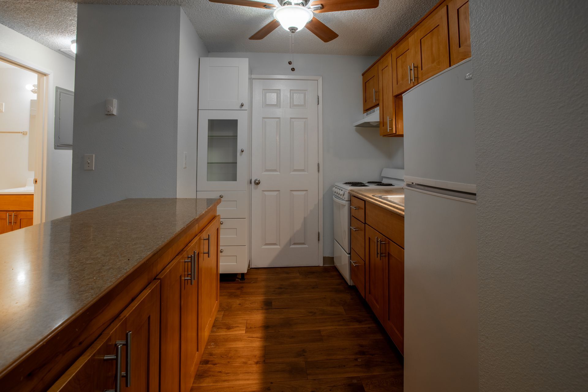 Kitchen with wooden cabinets and countertops, white appliances, a door, and a ceiling fan.