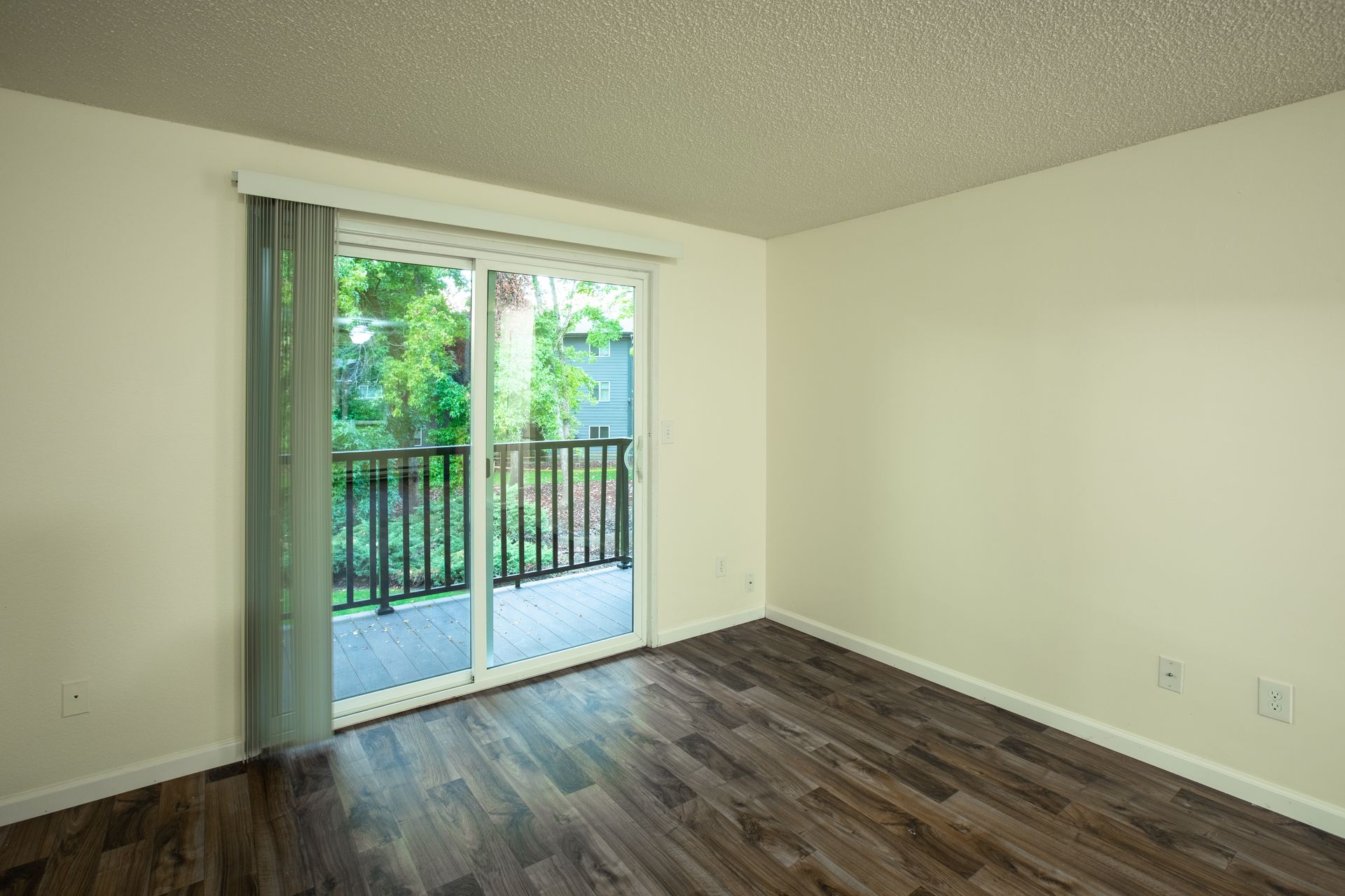 Empty room with dark wood floor, sliding glass door to balcony, cream walls.