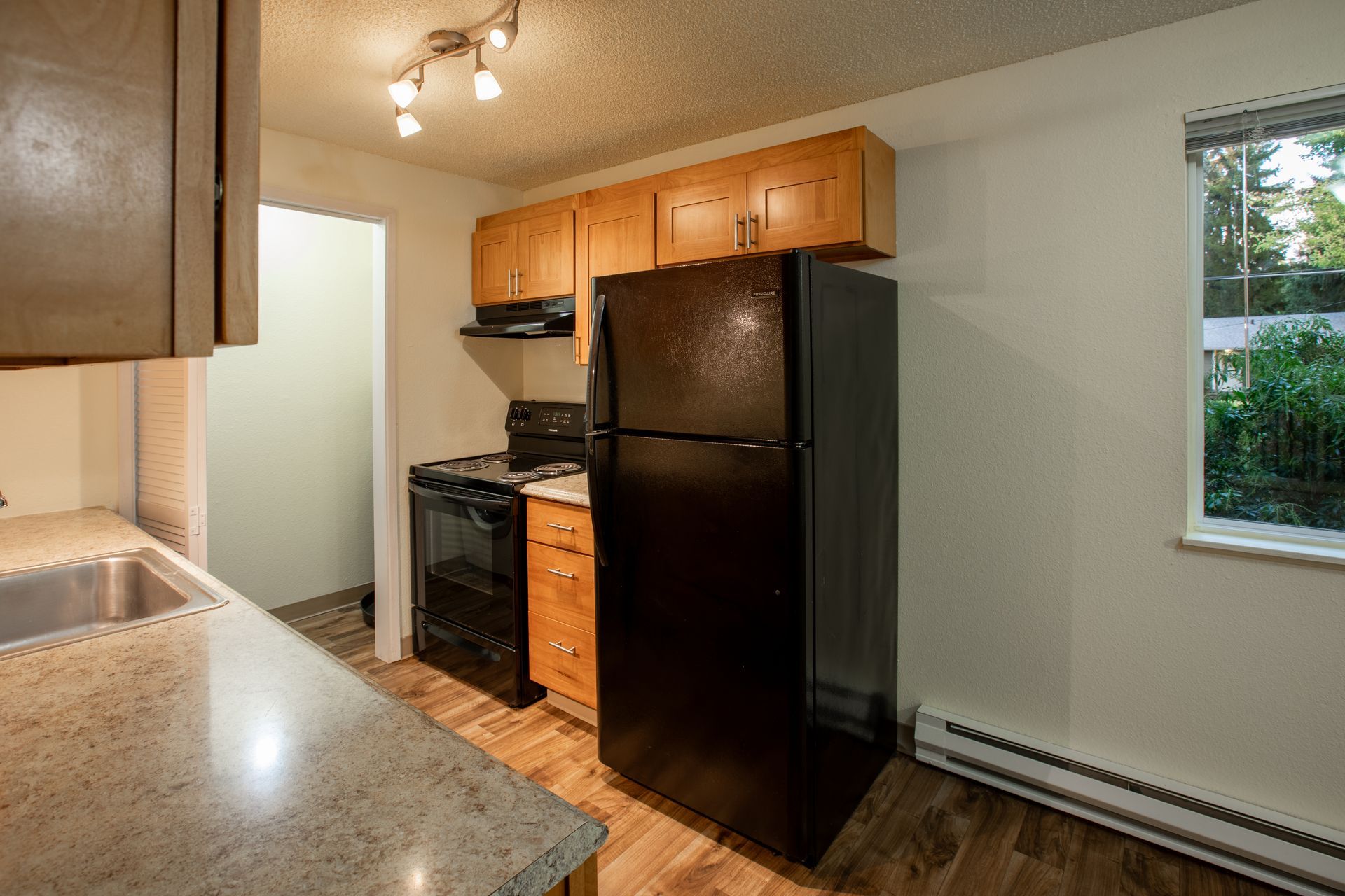 Kitchen with black refrigerator, stove, wooden cabinets, and a sink.