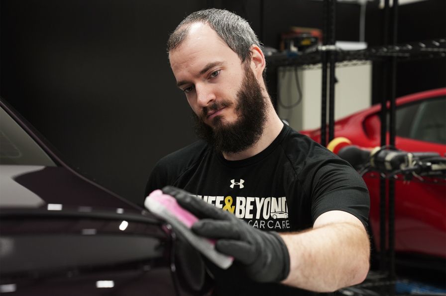 A man with a beard is polishing a car with a sponge.