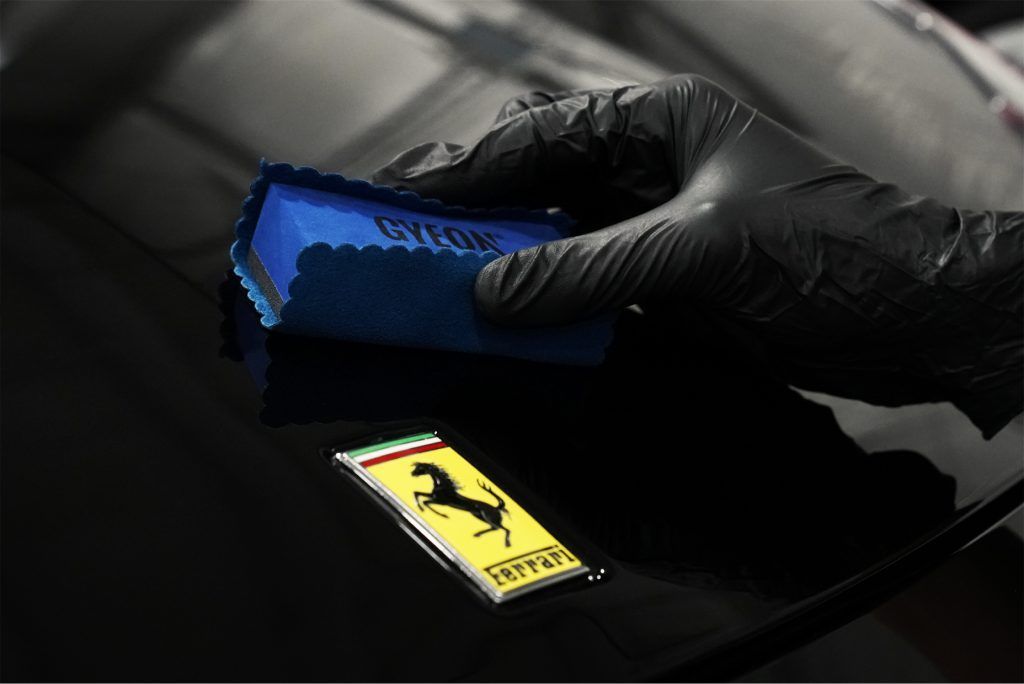 A person is polishing a ferrari emblem with a sponge.