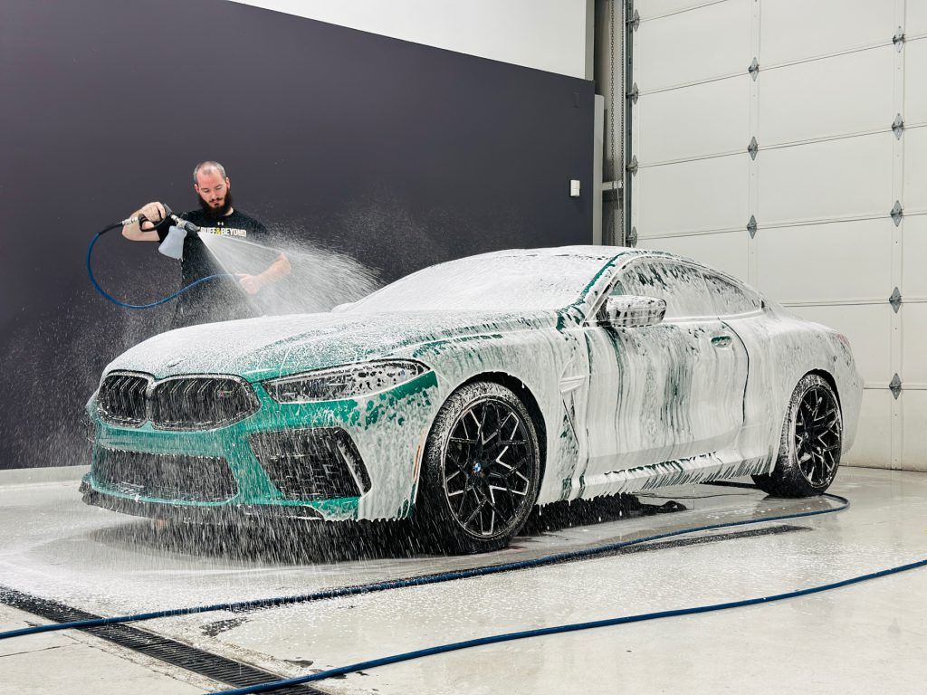 A man is washing a car with foam in a garage.