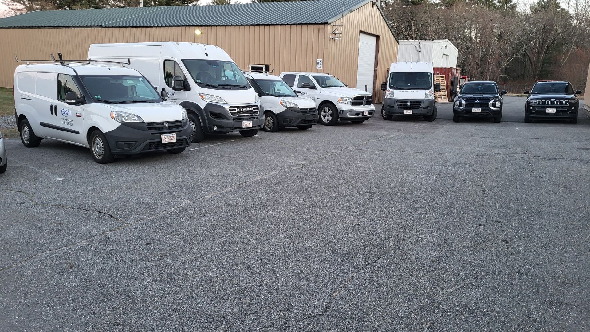 A row of white vans are parked in a gravel lot in front of a building.