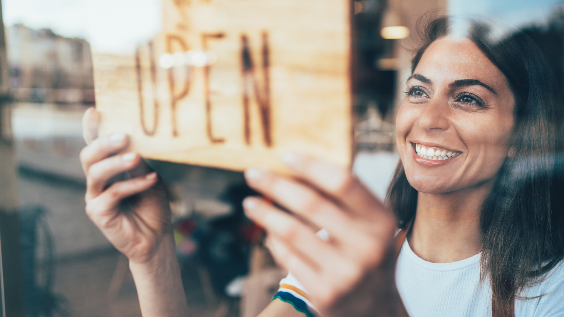 A woman is holding an open sign in front of a window.